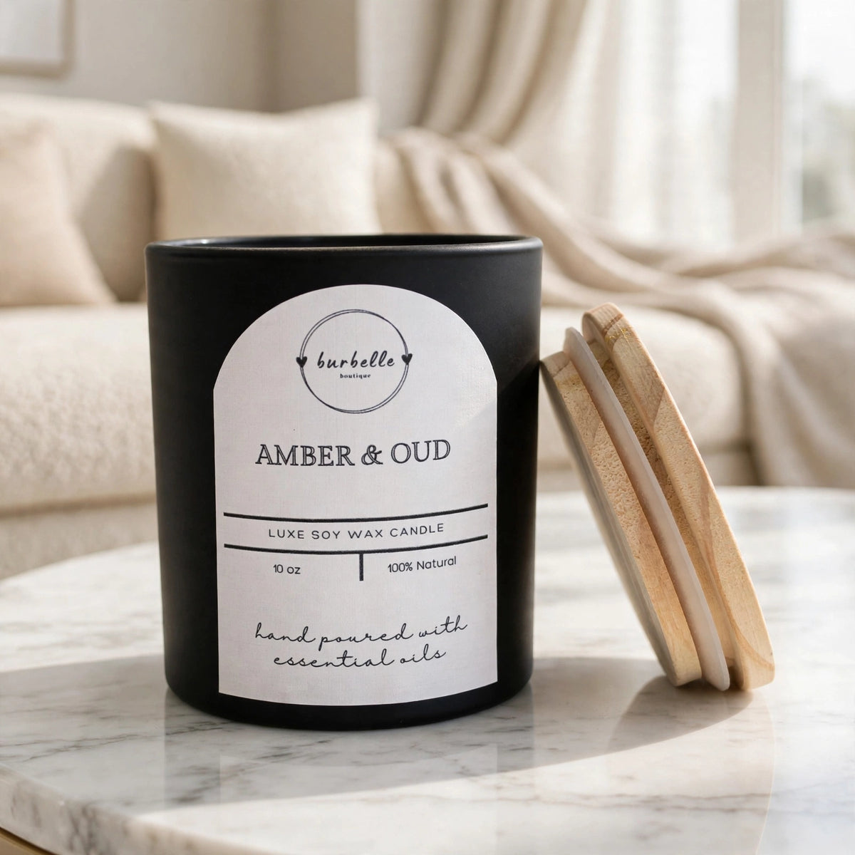 Amber & Oud luxe soy wax candle in a black jar with the wooden lid leaning beside it, styled on a marble coffee table in a bright living room. Clean non-toxic candle hand poured with 100% essential oils, Burbelle Boutique.