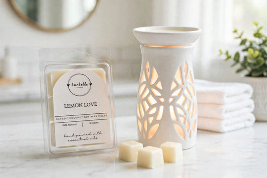 Lemon Love Classic coconut soy wax melts clamshell beside a lit white ceramic wax warmer with loose wax cubes